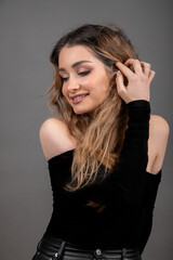Fototapeta premium Young female model with long loose hair smiles coquettishly, lowering her eyes. Studio grey background. Beauty salon. 