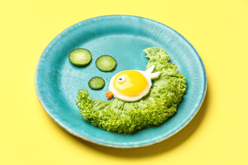 Plate with funny children's breakfast in shape of fish on yellow background