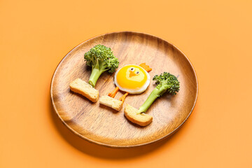 Plate with funny children's breakfast in shape of chick on orange background