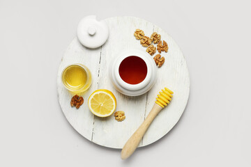 Board with jar of sweet honey, walnuts, lemon and dipper on light background