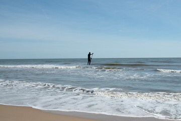 Fototapeta na wymiar A person in a wetsuit, Standing up and paddle boarding in the Atlantic Ocean, VA. Beach USA. 
