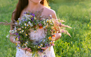 wreath of meadow flowers in hands girl, summer natural blurred background. floral traditional decor...