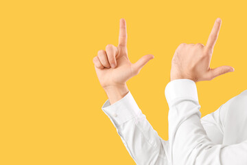 Young businessman showing loser gesture on yellow background