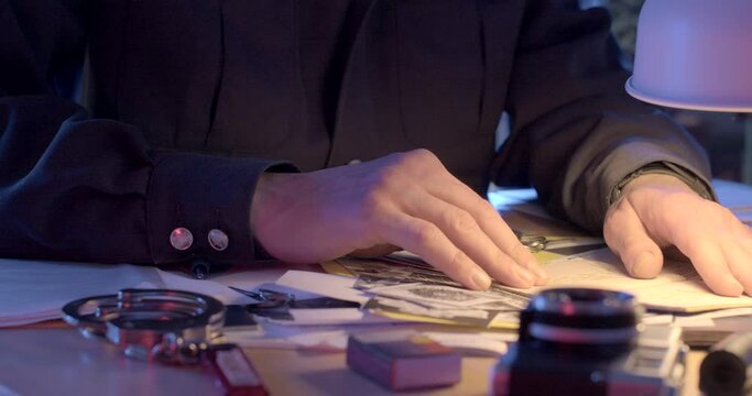 The detective's hands control the passport document at the KGB desk, he is looking for evidence of forged documents. Handcuffs on the table.