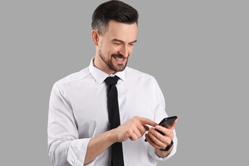 Handsome businessman using mobile phone on grey background