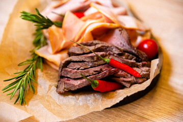 Sliced roast beef, sliced red meat with rosemary and chili pepper, thinly sliced ham wrapped in craft paper on wooden board