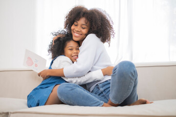African American daughter give her mother mother's day card with love, mom embrass her kid with love feeling, relationship with parent and child in family.