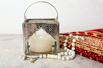 Fototapeta na wymiar Muslim lamp with burning candle, prayer beads and mat on table near white wall