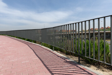 Brick pathway with metal railing casting shadow over them in an urban park