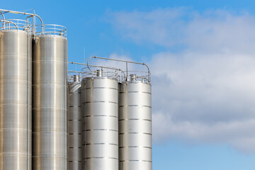 Stainless steel silos against the blue sky. Warehouses for storage of plastics and bulk grains.
