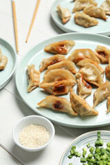 Plates with tasty Chinese jiaozi, onion and sauce on white wooden background