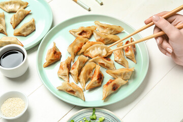 Woman eating tasty Chinese jiaozi on white wooden table