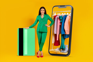 Happy lady standing near huge smartphone with clothing rail on display and giant credit card, using...