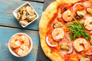 Slate board with tasty seafood pizza and ingredients on blue wooden background, closeup