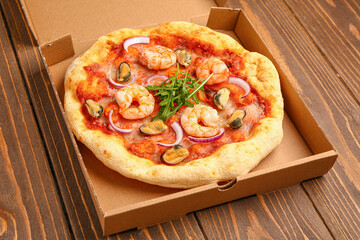 Cardboard box with tasty seafood pizza on wooden background