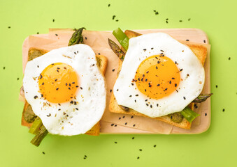 Delicious sandwiches with fried eggs and asparagus on green background