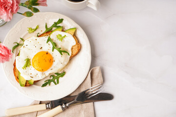 Delicious sandwich with fried egg, avocado and arugula on light background