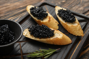 Tasty bruschettas with black caviar on wooden background