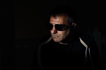 Hair stubbled adult male face wearing aviator style sun glasses in a dark room