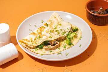 Tasty omelet with broccoli and mushrooms on orange background