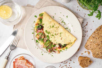 Tasty omelet with ham and greens on light table