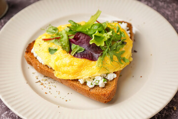 Plate with tasty scrambled eggs sandwich on grey grunge background