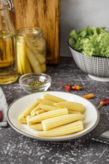 Plate with canned baby corn cobs on grey grunge background
