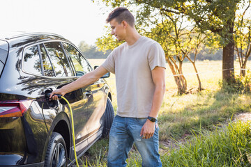 Obraz premium Young man plugging in the charger in a black electric car, renewable energy concept