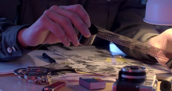 Checking the negative film of the camera for evidence of compromising evidence. Twisting the babin and winding in the hands of the secret police. Detective's workplace.