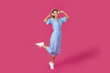 Glad middle aged european blonde lady with closed eyes in wireless headphones dances, listens to music