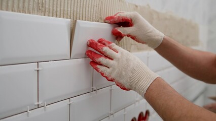 Tiler hands in the process of laying white rectangular tiles on bathroom wall. Repair of apartments...