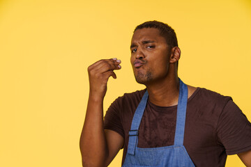 Stylish African American cook wearing blue apron sends kiss with his fingers in Italian manner,...