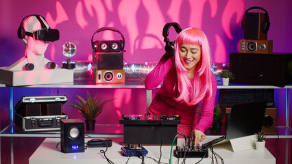 Cheerful musician playing techno music at turntables, enjoying having fun and dancing in club during party. Artist with pink hair performing remix sound using professional audio equipment