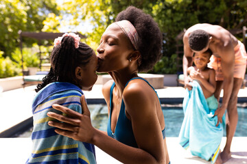 African american mother kissing on daughter's forehead and father wiping son at poolside in resort