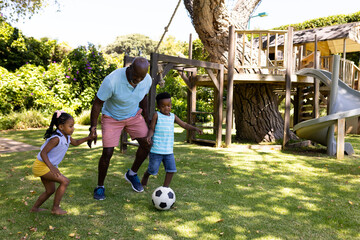 African american grandfather playing soccer with cheerful grandchildren in park - obrazy, fototapety, plakaty