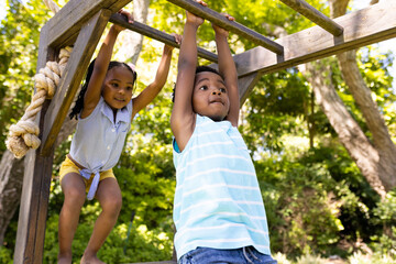 Low angle view of african american sister and brother hanging on monkeys bars at playground