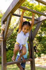 Obraz premium Low angle view of african american girl hanging on monkeys bars at playground
