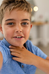 Closeup portrait of caucasian cute boy with gray eyes smiling and touching neck at home