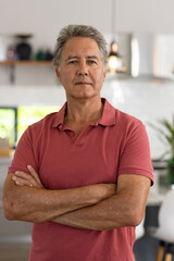 Portrait of serious caucasian senior man with arms crossed standing at home, copy space