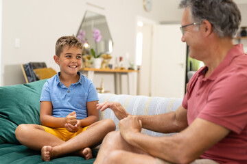 Caucasian cute boy smiling and communicating with grandfather in sign language while sitting on sofa