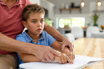 Midsection of caucasian grandfather assisting blind grandson in reading braille book at home - obrazy, fototapety, plakaty
