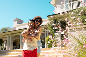 Portrait of happy diverse couple standing outside the house, embracing and smiling