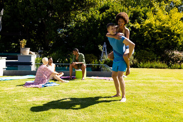 Happy diverse couple giving each other piggyback rides and smiling in garden