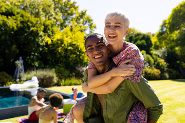 Portrait of happy diverse couple giving each other piggyback rides and smiling in garden