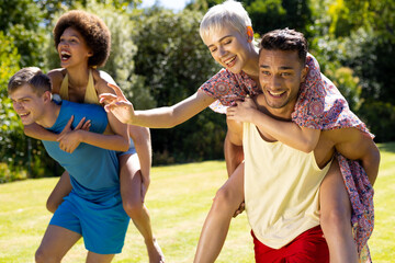 Fototapeta premium Happy diverse group of friends giving each other piggyback rides in garden