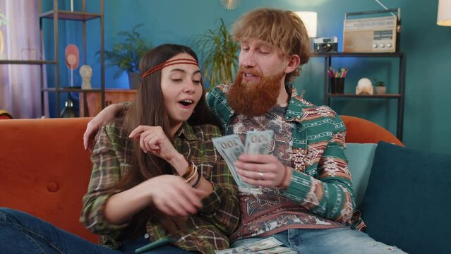 Planning family budget. Family married hippie couple man woman counting money cash, use smartphone calculate domestic bills at home. Husband wife satisfied of income for planned vacation, gifts