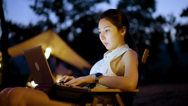 Asian woman using a laptop working remotely while camping in the forest