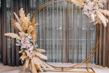 Obraz premium A beautiful round arch made of reeds, roses, wild flowers stands in the restaurant at the ceremony. wedding photography.