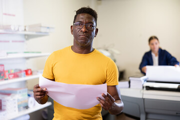 Portrait of positive male employee of a printing house with projects in hands