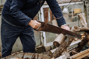 A man in a robe, a lumberjack, a worker saws a tree, a log with a hand saw, outdoors, in nature, at a sawmill. Photo, close-up.